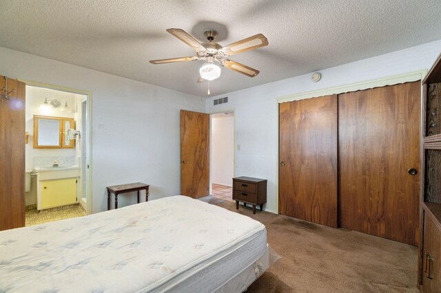 carpeted bedroom with a closet, ceiling fan, a textured ceiling, a sink, and ensuite bath