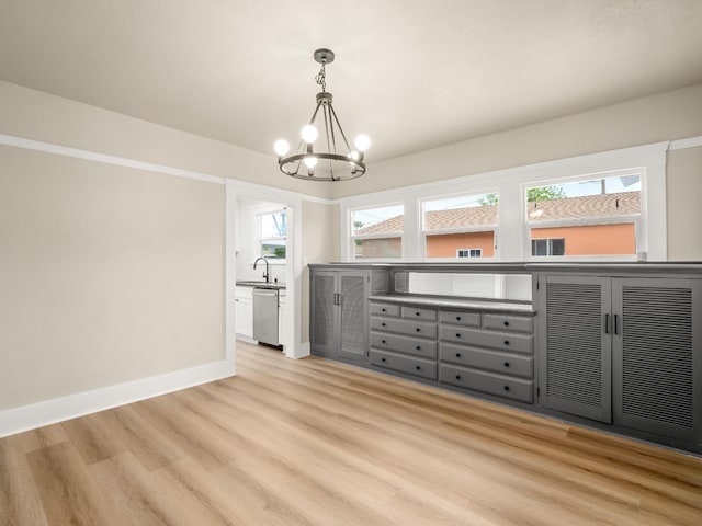 unfurnished dining area with a sink, baseboards, light wood-style flooring, and a chandelier