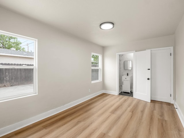 unfurnished bedroom featuring baseboards, light wood-style flooring, and connected bathroom