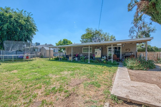 back of property featuring a trampoline, a lawn, fence, an outdoor structure, and a shed