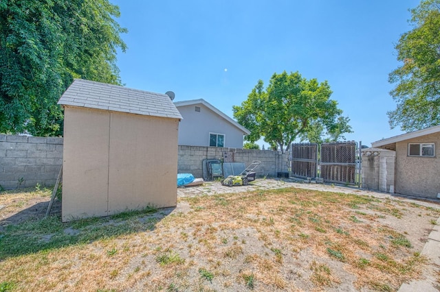 view of yard featuring a storage unit, a fenced backyard, an outbuilding, and a gate