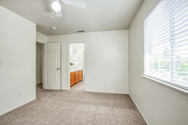 unfurnished bedroom with light colored carpet, a ceiling fan, baseboards, ensuite bathroom, and visible vents