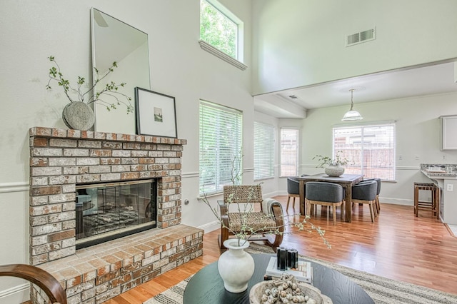 living area featuring a brick fireplace, visible vents, a wealth of natural light, and wood finished floors