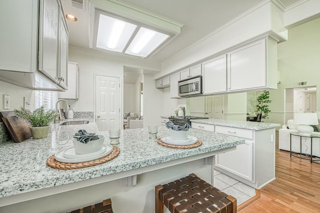 kitchen with crown molding, light stone countertops, a sink, a peninsula, and stainless steel microwave