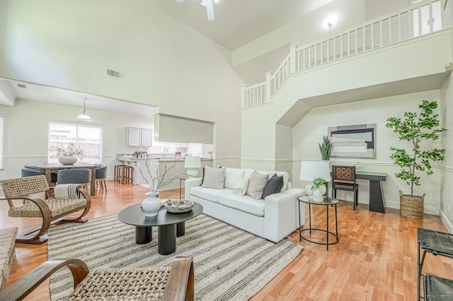 living room featuring visible vents, light wood finished floors, a towering ceiling, and baseboards