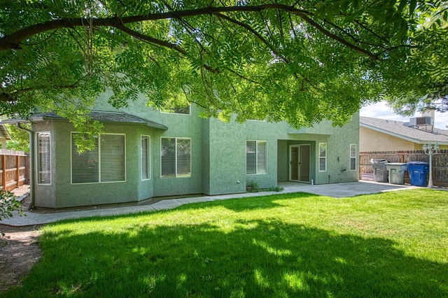 rear view of property featuring fence, a patio, stucco siding, and a lawn
