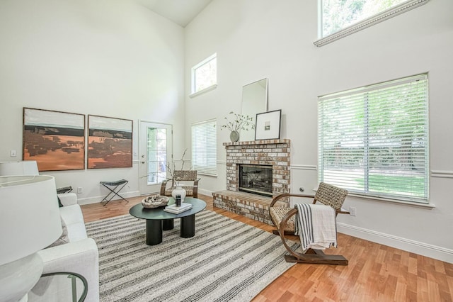 living area with a fireplace, baseboards, wood finished floors, and a towering ceiling