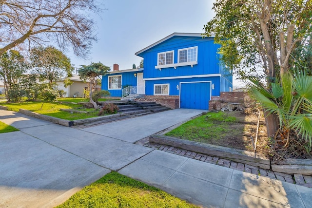 split level home featuring a garage, a front yard, a chimney, brick siding, and concrete driveway