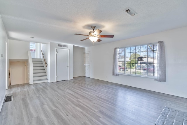 unfurnished living room with stairs, a ceiling fan, visible vents, and wood finished floors