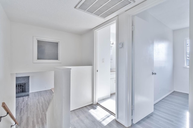 hall featuring visible vents, wood finished floors, baseboards, a textured ceiling, and an upstairs landing