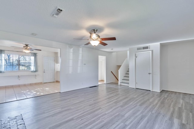 unfurnished living room with visible vents, ceiling fan, wood finished floors, and stairway