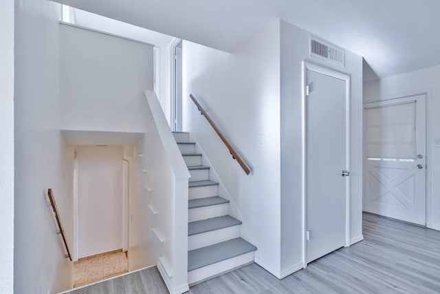 staircase with baseboards, visible vents, and wood finished floors