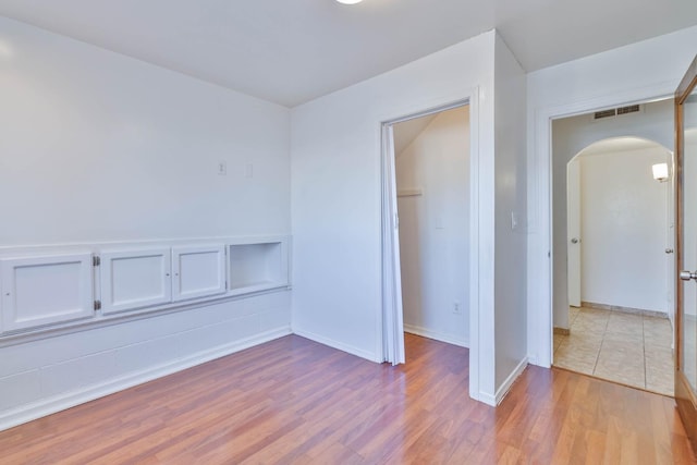 empty room with visible vents, arched walkways, baseboards, and wood finished floors