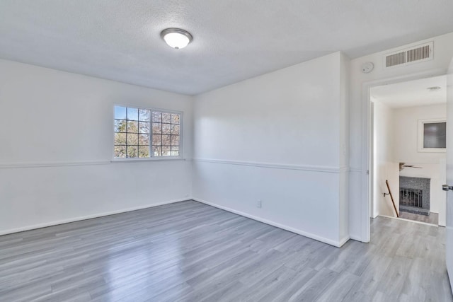 spare room featuring a textured ceiling, a brick fireplace, wood finished floors, and visible vents