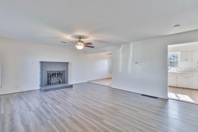 unfurnished living room with a brick fireplace, ceiling fan, visible vents, and light wood-style floors