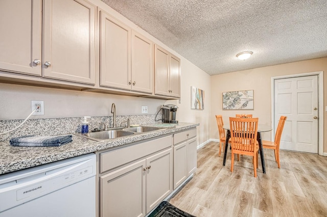 kitchen featuring white dishwasher, a sink, light wood-style floors, a textured ceiling, and baseboards