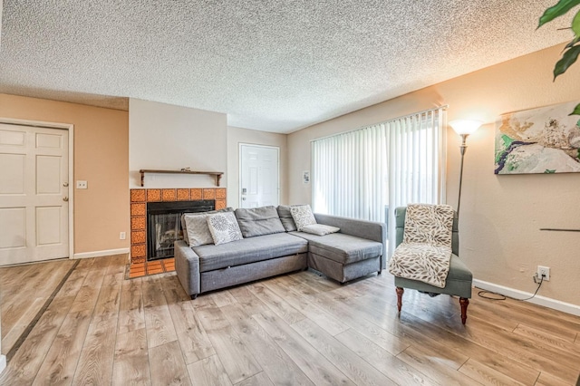 living room with a fireplace, a textured ceiling, baseboards, and light wood-style floors