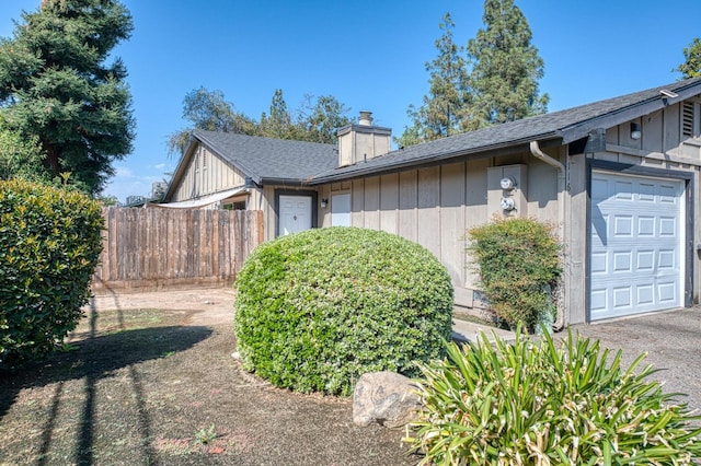 view of property exterior featuring fence, a chimney, an attached garage, and roof with shingles
