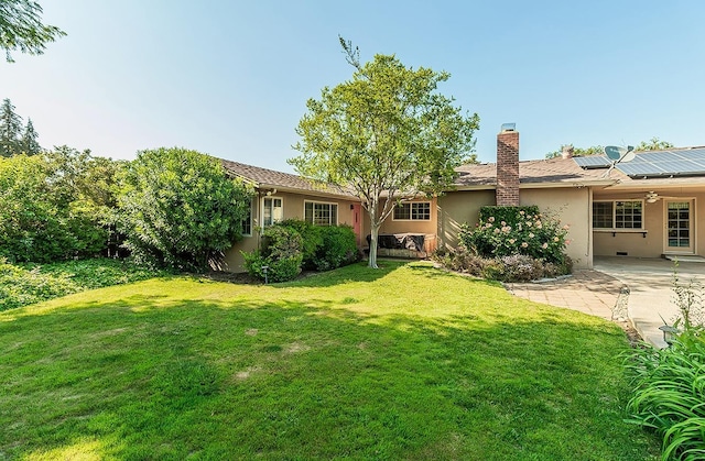 back of property with stucco siding, a chimney, a patio area, a yard, and solar panels