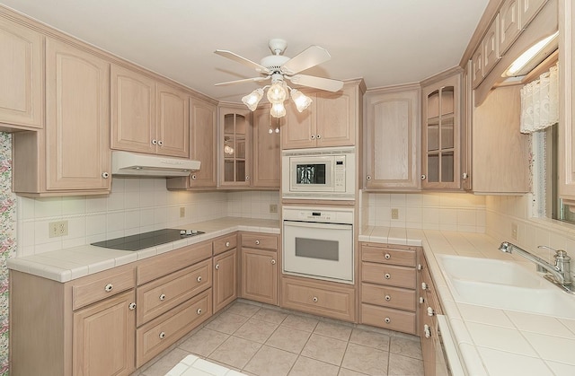 kitchen with white appliances, tile countertops, under cabinet range hood, tasteful backsplash, and a sink