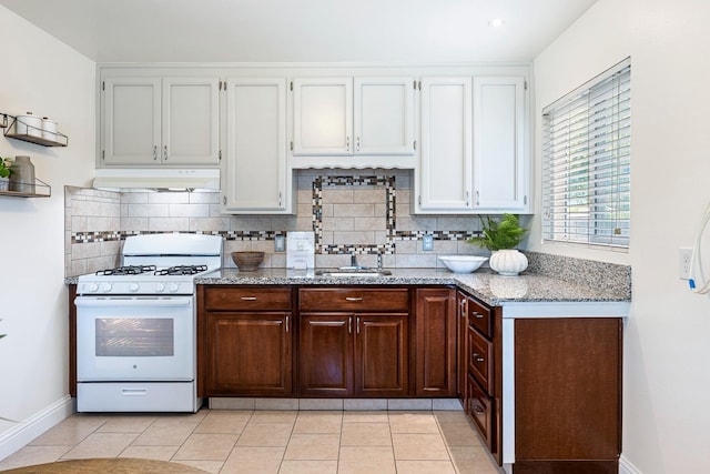 kitchen with decorative backsplash, under cabinet range hood, white range with gas stovetop, and light stone countertops
