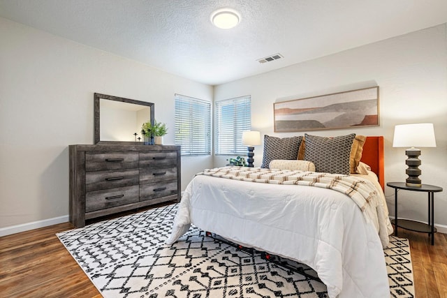 bedroom with a textured ceiling, baseboards, visible vents, and wood finished floors