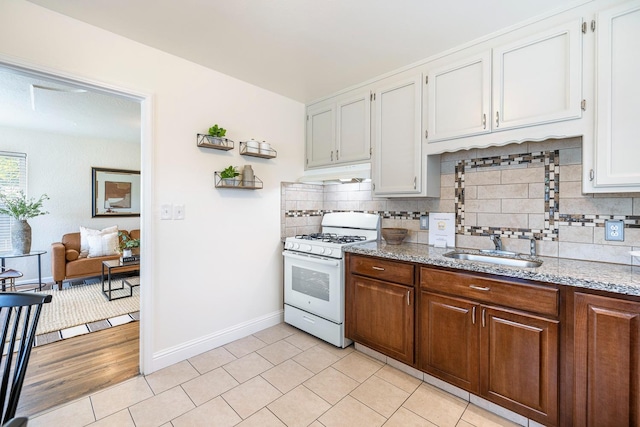 kitchen with a sink, tasteful backsplash, white range with gas stovetop, and under cabinet range hood