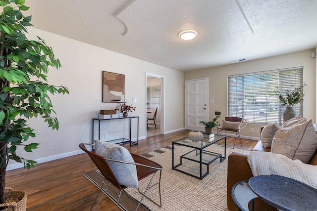 living area featuring visible vents, baseboards, a textured ceiling, and wood finished floors