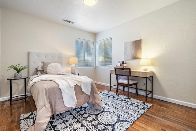bedroom featuring visible vents, baseboards, a textured wall, and wood finished floors
