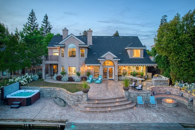 rear view of house with french doors, a hot tub, a balcony, an outdoor fire pit, and a patio