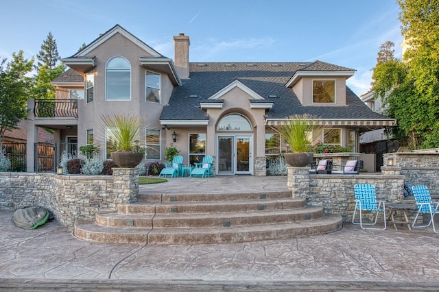 rear view of house with a chimney, outdoor dry bar, a patio area, a shingled roof, and stucco siding