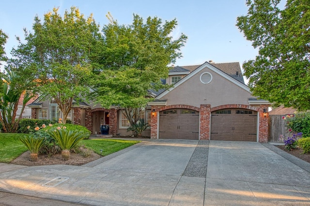 view of front of house with stucco siding, brick siding, driveway, and a garage