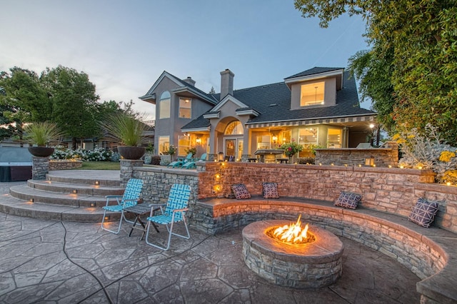 back of property with a fire pit, a patio area, a chimney, and roof with shingles