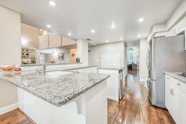 kitchen featuring freestanding refrigerator, a peninsula, a kitchen island, a sink, and dark wood finished floors