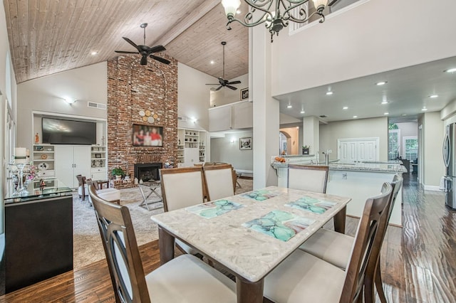 dining room featuring built in features, a brick fireplace, high vaulted ceiling, dark wood-type flooring, and ceiling fan with notable chandelier