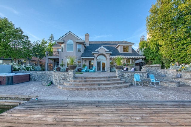 exterior space with a hot tub, an outdoor fire pit, a chimney, a balcony, and a patio