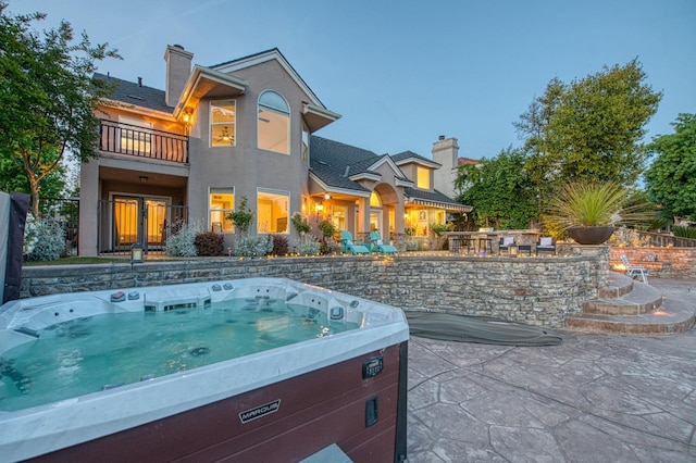 back of house with a hot tub, a chimney, a balcony, and stucco siding