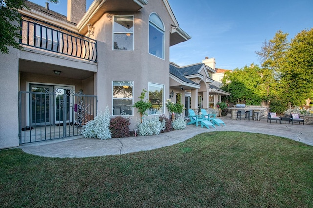rear view of property with stucco siding, a chimney, a balcony, a patio, and a yard