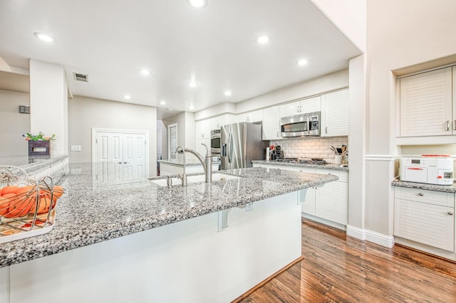 kitchen featuring a breakfast bar area, visible vents, appliances with stainless steel finishes, wood finished floors, and a sink