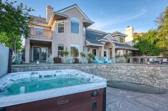 rear view of property with a hot tub, stucco siding, a chimney, a patio area, and a balcony