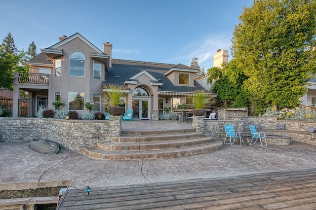 view of front of property featuring a chimney, a patio area, stucco siding, and a balcony