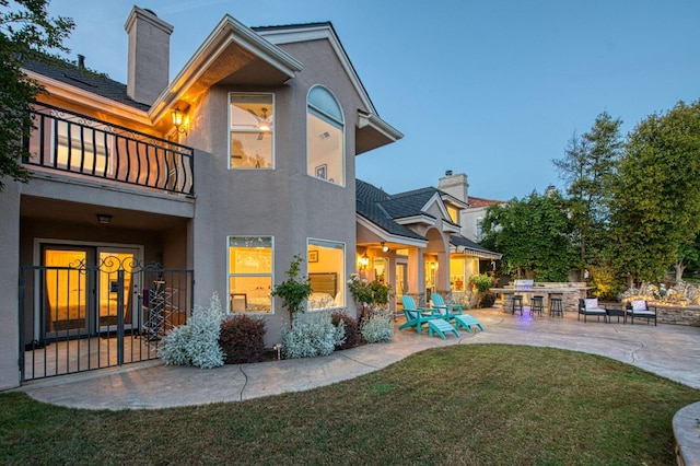 rear view of house featuring stucco siding, a chimney, a patio area, a balcony, and a yard