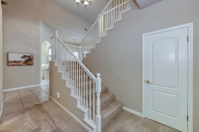 stairs with arched walkways, baseboards, carpet floors, and a chandelier
