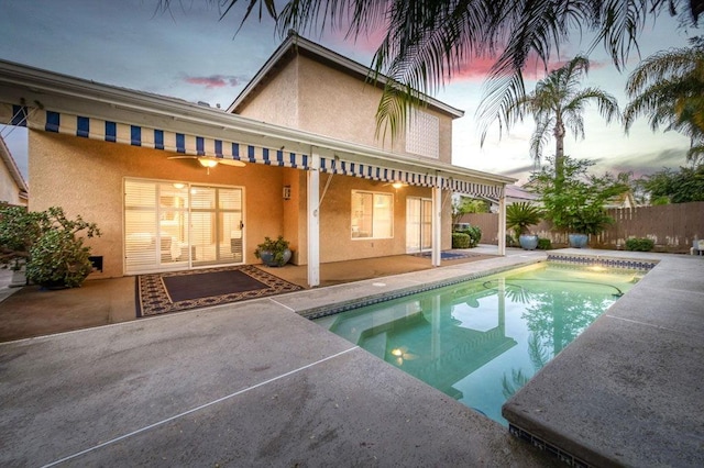 back of house at dusk featuring a fenced in pool, a fenced backyard, a patio area, and stucco siding