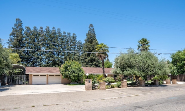 view of property hidden behind natural elements with concrete driveway, a tiled roof, and fence