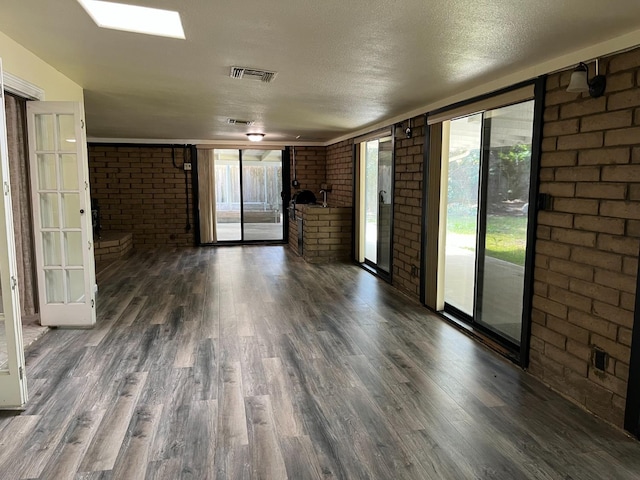unfurnished living room featuring brick wall, dark wood-style floors, and a healthy amount of sunlight