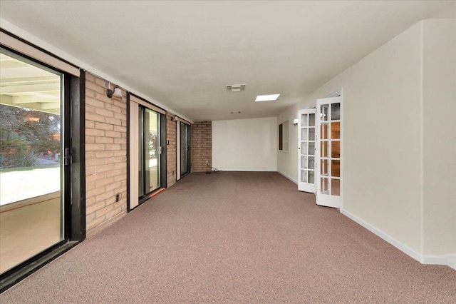 carpeted spare room featuring baseboards, brick wall, and visible vents