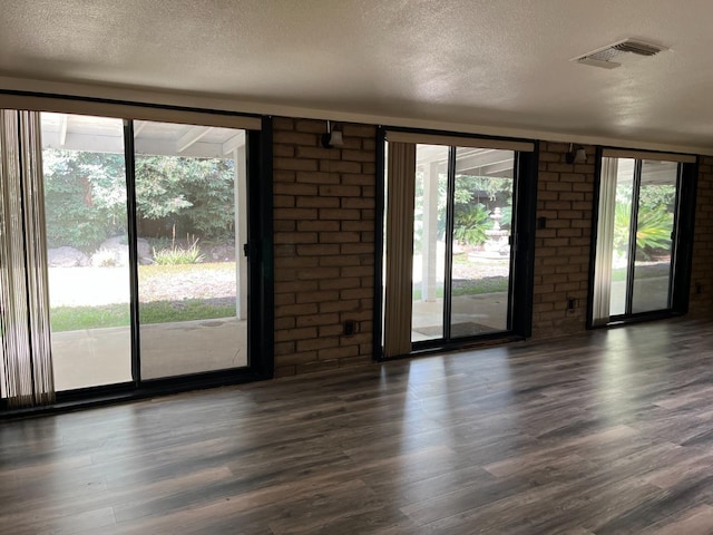 empty room featuring a textured ceiling, visible vents, dark wood-style floors, and brick wall