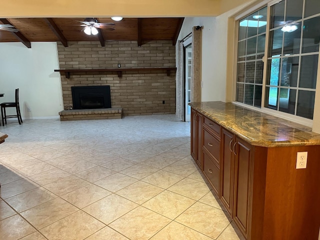 interior space with wood ceiling, a ceiling fan, a brick fireplace, beam ceiling, and dark stone counters