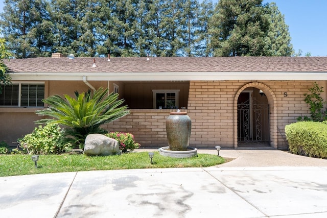 entrance to property with a shingled roof and brick siding